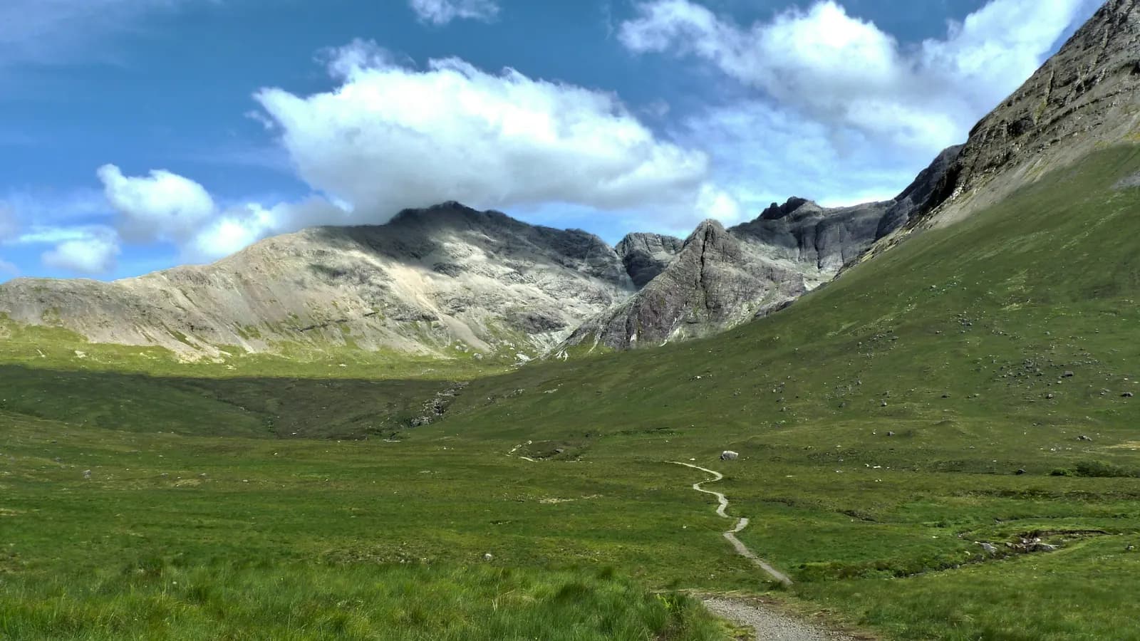A gravel path leading through a green valley towards rocky mountains