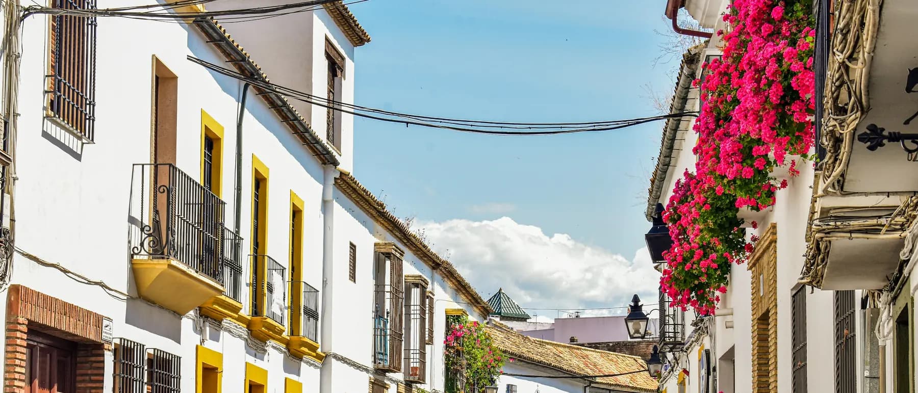 A cobblestone street of white houses with yellow trim and flower-filled balconies in Córdoba