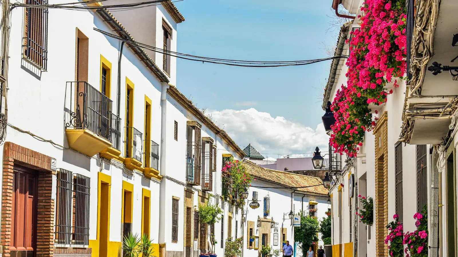 A cobblestone street of white houses with yellow trim and flower-filled balconies in Córdoba