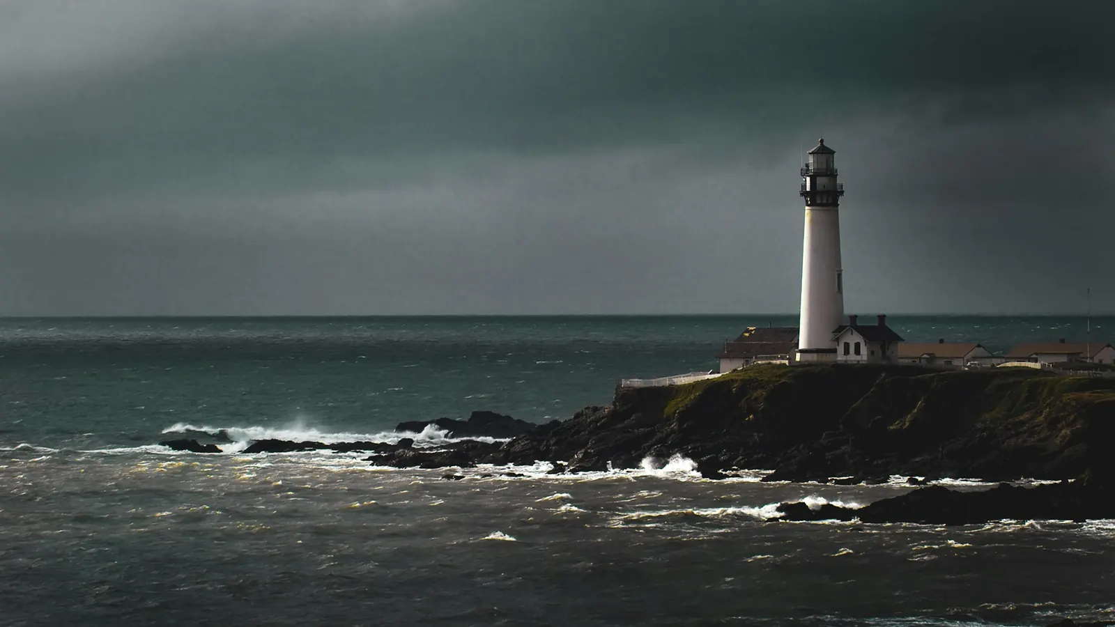 A white lighthouse on a rocky headland above a grey, choppy sea