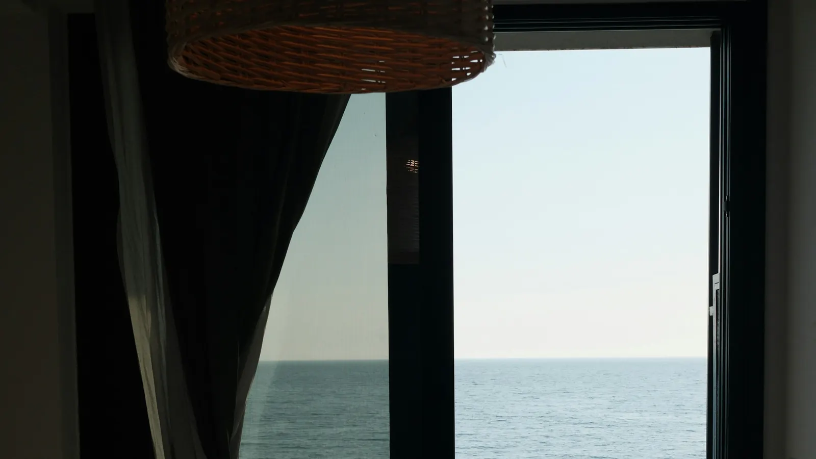 A calm sea seen through the open balcony door of a holiday bedroom